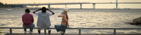 Header of three teenagers, including Black boy and Caucasian girl, sitting on railing by waterfront,...