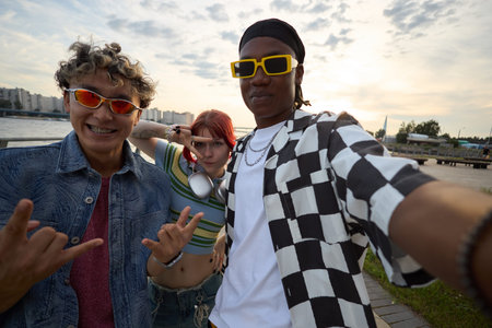 Portrait of diverse group of teenagers posing for selfie outdoors, smiling and gesturing with hands,...