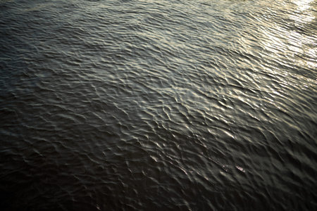 Surface of rippling water reflecting sunlight, creating textured pattern across entire frame,...