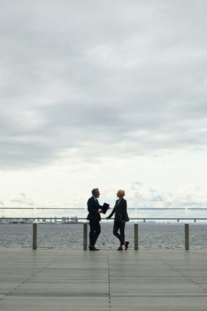 Mature Caucasian male and female business partners in formal wear standing and talking on promenade...