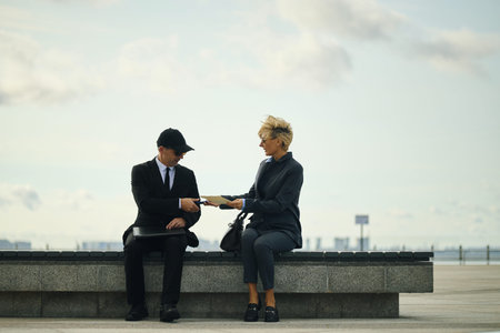 Middle aged Caucasian man in suit and cap handing document to mature woman with short blond hair...