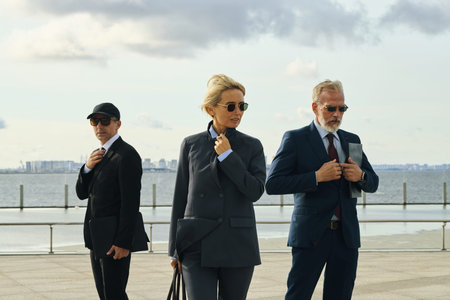 Caucasian mature businesswoman and two male colleagues in suits and sunglasses man standing outdoors...