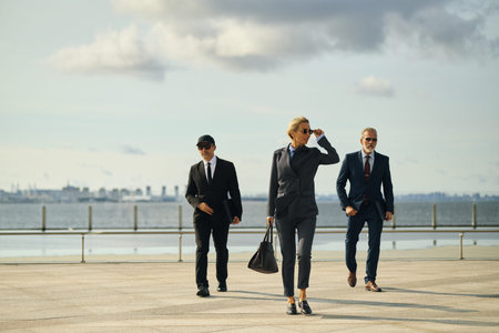 Caucasian middle aged businesswoman in business suit and sunglasses walking confidently outdoors...