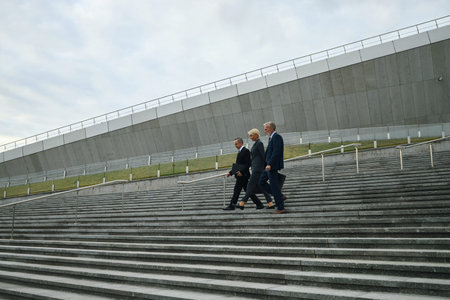 Three middle aged Caucasian corporate colleagues walking down wide outdoor concrete steps in...