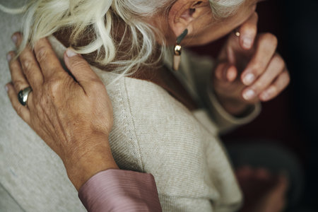 Senior Caucasian woman being comforted by friend placing hand on shoulder, showing emotional support and connection, partial view, during grief or bereavementの写真素材