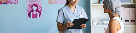 Header of Young Caucasian female nurse holding clipboard, talking with middle aged Caucasian woman wearing headscarf, in medical office, discussing cancer diagnosis and treatment optionsの写真素材
