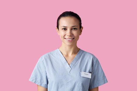 Portrait of young adult Caucasian female nurse, wearing medical scrubs, smiling at camera, standing...