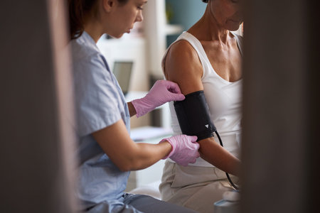 Middle aged Caucasian woman sitting while young adult Caucasian female nurse measuring blood...