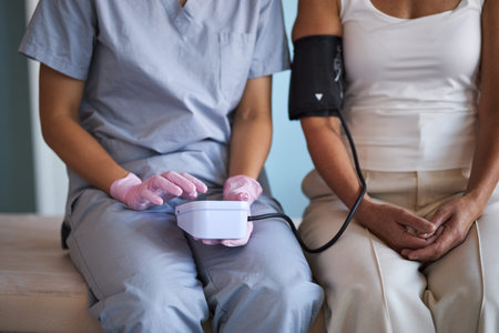 Middle aged Caucasian woman sitting on examination table having blood pressure measured by young...