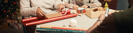Middle aged Caucasian woman and young adult Caucasian woman, wrapping Christmas gifts and writing...