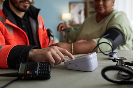 Middle aged male paramedic operating digital blood pressure monitor while middle aged woman sitting...