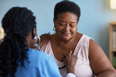 Senior Black woman sitting while female healthcare worker examining chest with stethoscope, patient...