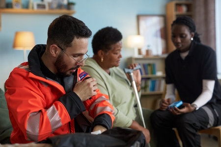Caucasian young adult man, wearing emergency responder uniform, speaking into radio, while Black...