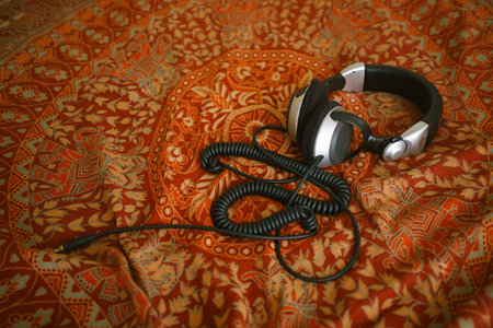 Overhead view showing professional over ear headphones with coiled cable resting on patterned fabric surface, emphasizing audio equipment on decorative textile backgroundの写真素材