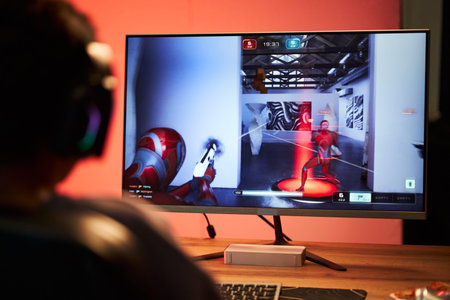 Teenage boy with headphones playing first shooter video game on computer monitor, sitting at desk,...