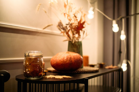 Still life showing autumn pumpkin, glass jar with preserved leaves, dried foliage in vase arranged on table, capturing seasonal Thanksgiving dinner decoration among friendsの写真素材