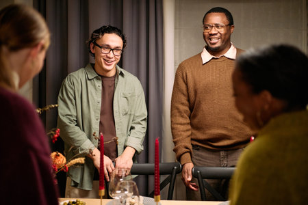 Young adult Asian man and young adult Black man standing and smiling among friends during...