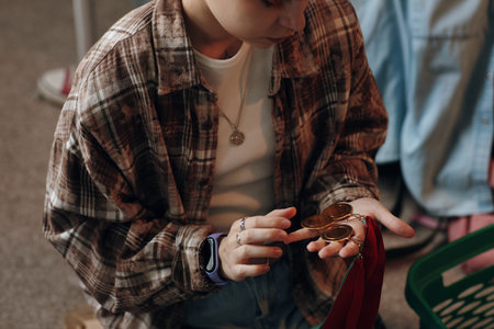 Caucasian teenage girl sitting in room holding several gold medals in hand, examining awards with thoughtful expression, wearing casual clothingの写真素材