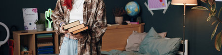 Header of teenage girl with long hair standing in bedroom holding stack of books, wearing casual clothing, engaging in reading activity, visible bed and study area in backgroundの写真素材