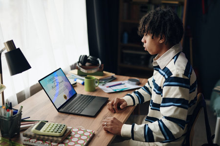 Teenage Black boy sitting at desk using laptop, receiving achievement certificate on study course...
