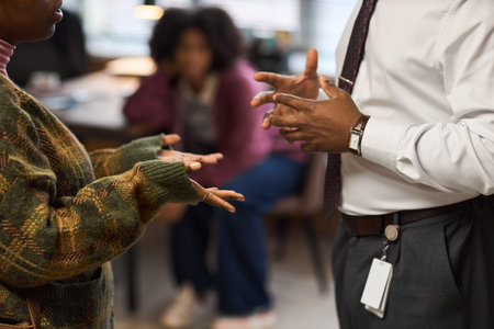 Middle aged man gesturing with hands while talking to young adult woman in office setting, blurred...