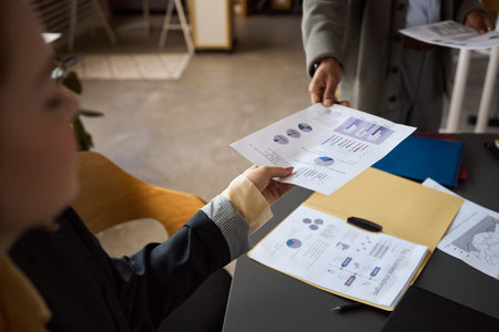 Caucasian young adult woman receiving business documents with charts and graphs from Black man...