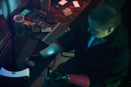 Young adult woman with short hair sitting at desk working on computer system, wearing cyberpunk...