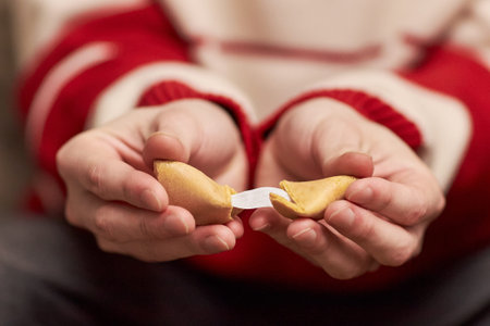 Adult hands breaking open fortune cookie with visible paper fortune slip, celebrating Tet holiday tradition, close up of fingers gently holding cookie in festive settingの写真素材
