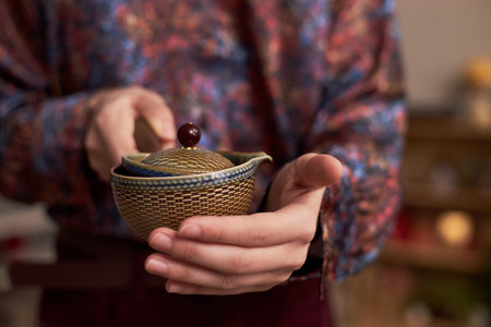 Asian young adult man holding traditional woven bowl with wooden lid and stick, performing ceremonial gesture during Tet holiday celebration, hands in focus, background blurredの写真素材