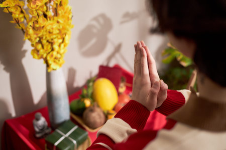 Young Asian woman clasping hands in prayer gesture in front of traditional holiday altar with fruit...
