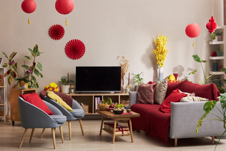 Living room decorated with red lanterns, festive ornaments, and yellow flowers for holiday celebration, coffee table displaying traditional food, television on wooden standの写真素材