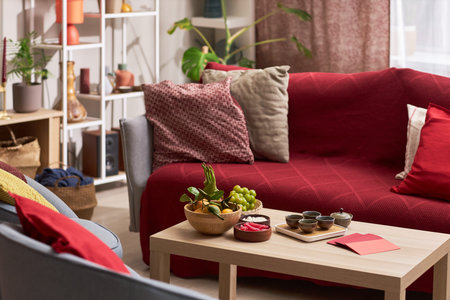 Living room decorated for Tet holiday featuring wooden table with fruit platter, tea set, red envelopes and snacks, sofa with red cushions and festive decorations in backgroundの写真素材