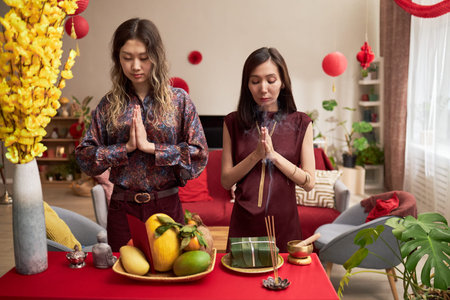 Two young adult Asian women standing with hands pressed together, performing traditional prayer...