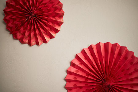 Two large red paper fans hanging on plain wall, traditional festive decorations commonly used during Tet holiday, geometric patterns creating vibrant celebratory atmosphereの写真素材