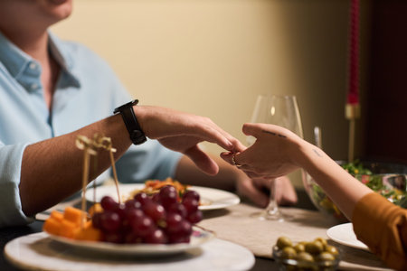 Caucasian man gently holding hand of young adult Caucasian woman across dinner table, both sitting...