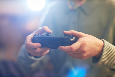 Caucasian teenager holding video game controller, focusing on hands and device during gaming session, background blurred, no face visible, emphasizing youth technology interactionの写真素材