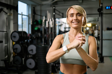 Portrait of smiling Caucasian middle aged woman clasping hands together in gym setting, engaging in...