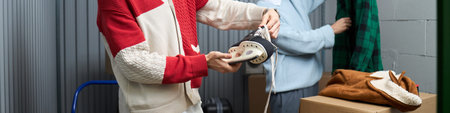 Young adult Caucasian man holding ice skate while standing in storage unit, another young adult man...