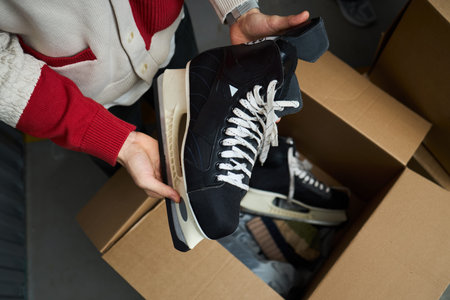 Caucasian young adult man holding pair of black ice hockey skates above open cardboard box,...
