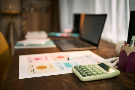 Closeup showing desk with financial charts, calculator, laptop and stationery arranged for lesson...