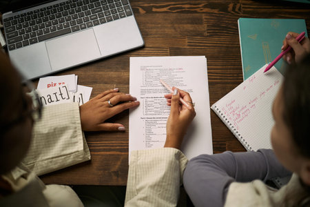 Caucasian female tutor assisting teenage girl with language lesson, both sitting at desk reviewing...