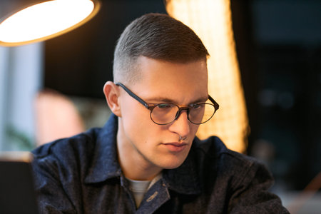 Portrait of young adult Caucasian man with short hair and glasses concentrating while working at...