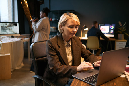 Caucasian woman typing on laptop in modern office, focusing on screen while middle aged Black woman...