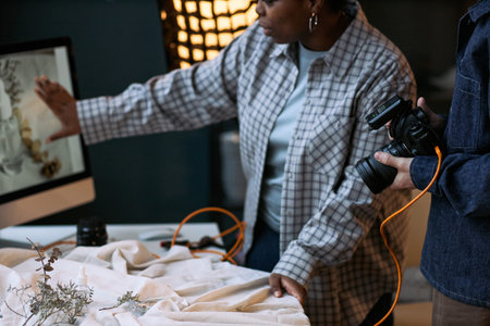 Black woman looking at photo on computer monitor while collaborating with young Caucasian man...