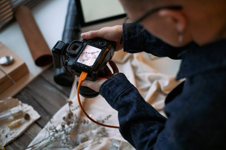 Young adult man holding digital camera, photographing flat lay arrangement on table, focusing on...