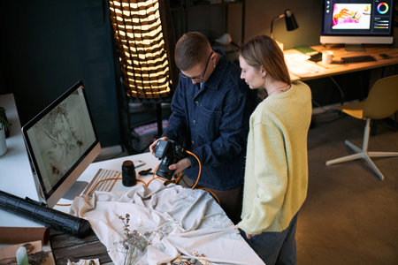 Young adult Caucasian man showing digital camera screen to young adult Caucasian woman while...