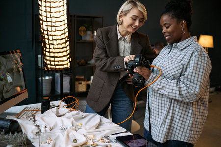Caucasian mature woman showing camera settings to Black young adult woman while standing together at...