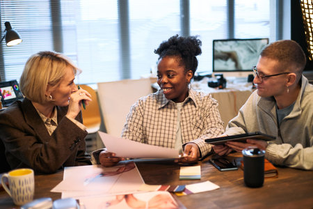 Middle aged Caucasian woman, young adult Black woman, young adult Caucasian man sitting at table...