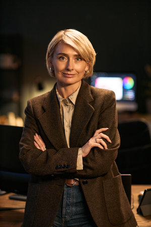 Portrait of middle aged Caucasian woman standing with arms crossed, smiling confidently while...