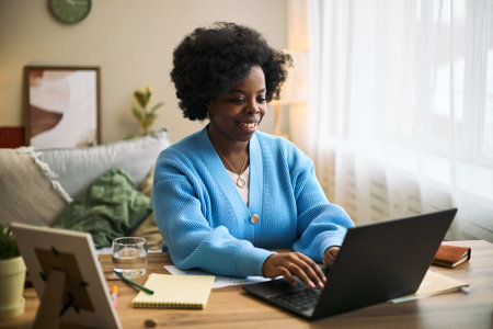 Young adult Black woman sitting at desk using laptop for health tracking or telemedicine...